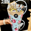 Bouquet of snacks in a floral cone with a visible brand logo, held by a person.